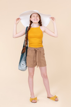 Teenage girl squeezing her eyes and adjusting white hat she's wearing