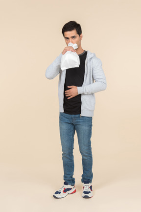 Молодой кавказский человек дышит в бумажный пакет