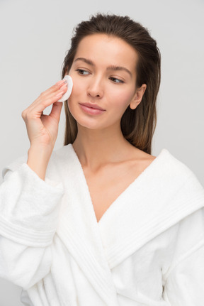 Beautiful young woman cleaning her face with cotton pad