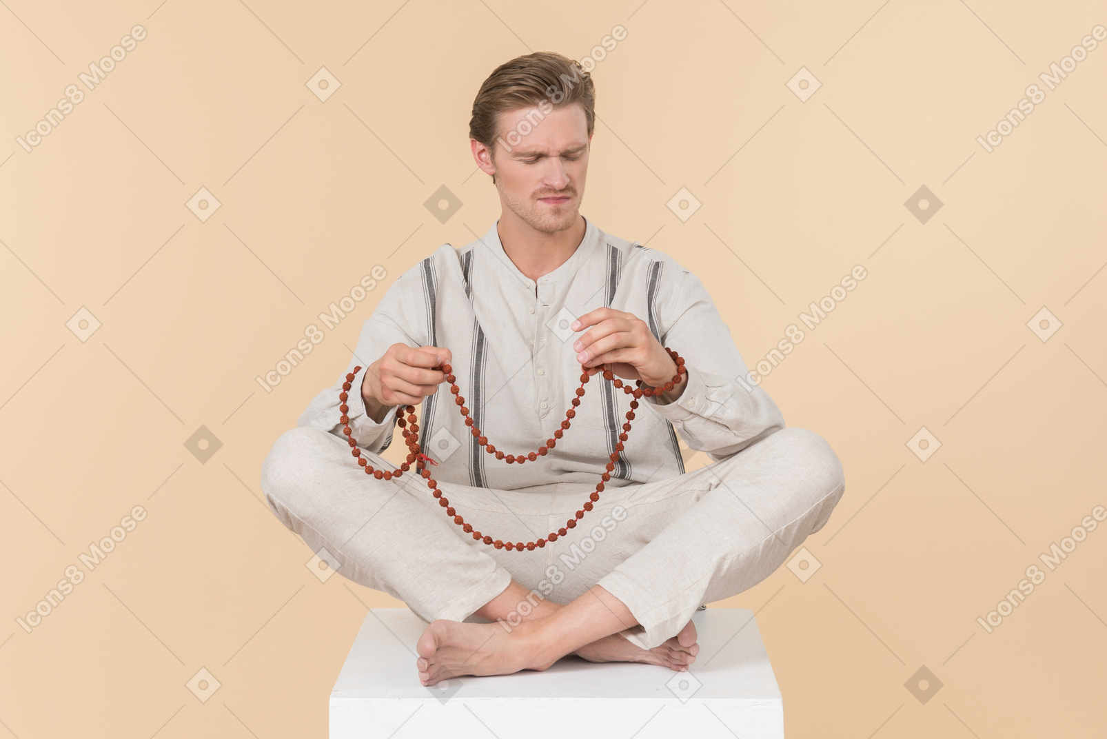 Young caucasian man sitting in lotus pose and putting on necklace