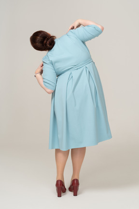 Вид сзади женщины в синем платье позирует с руками на плечах