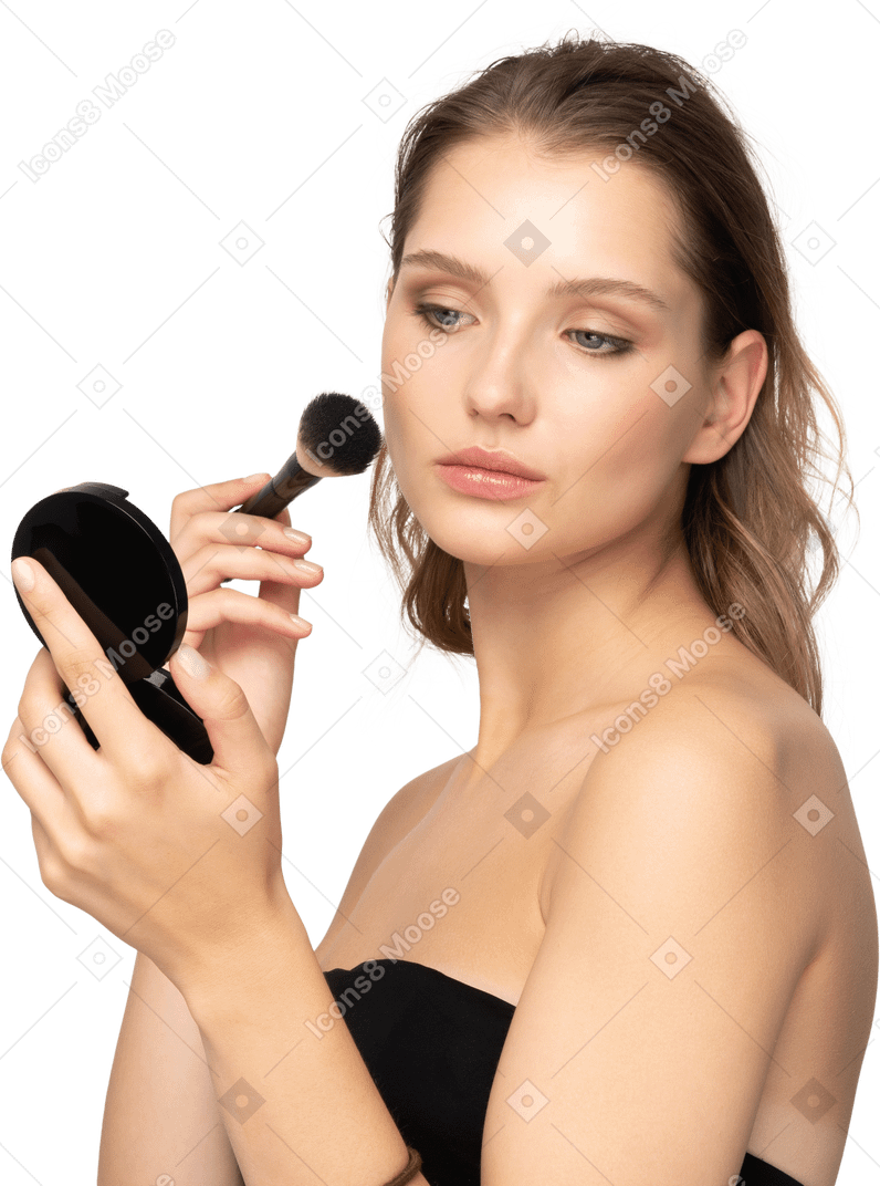 Vista lateral de uma jovem aplicando pó facial enquanto segura um espelho