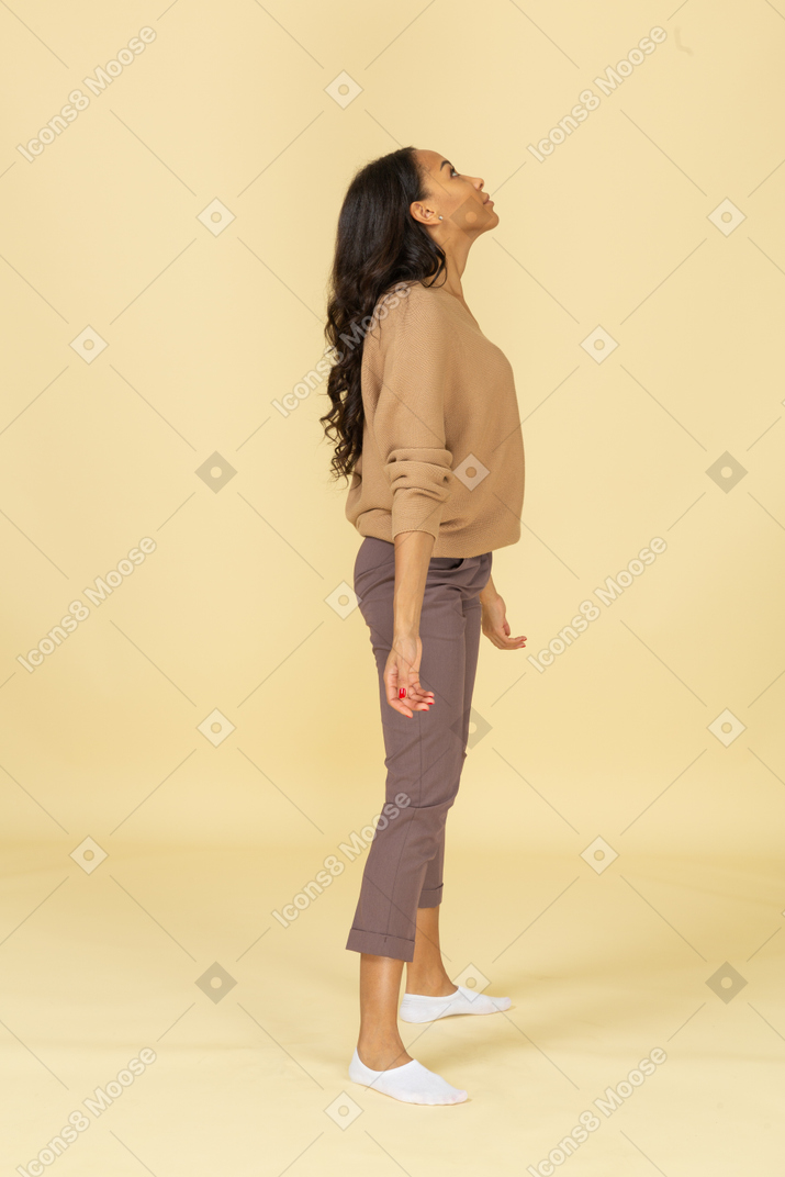 腕を広げて立っている浅黒い肌の若い女性の側面図