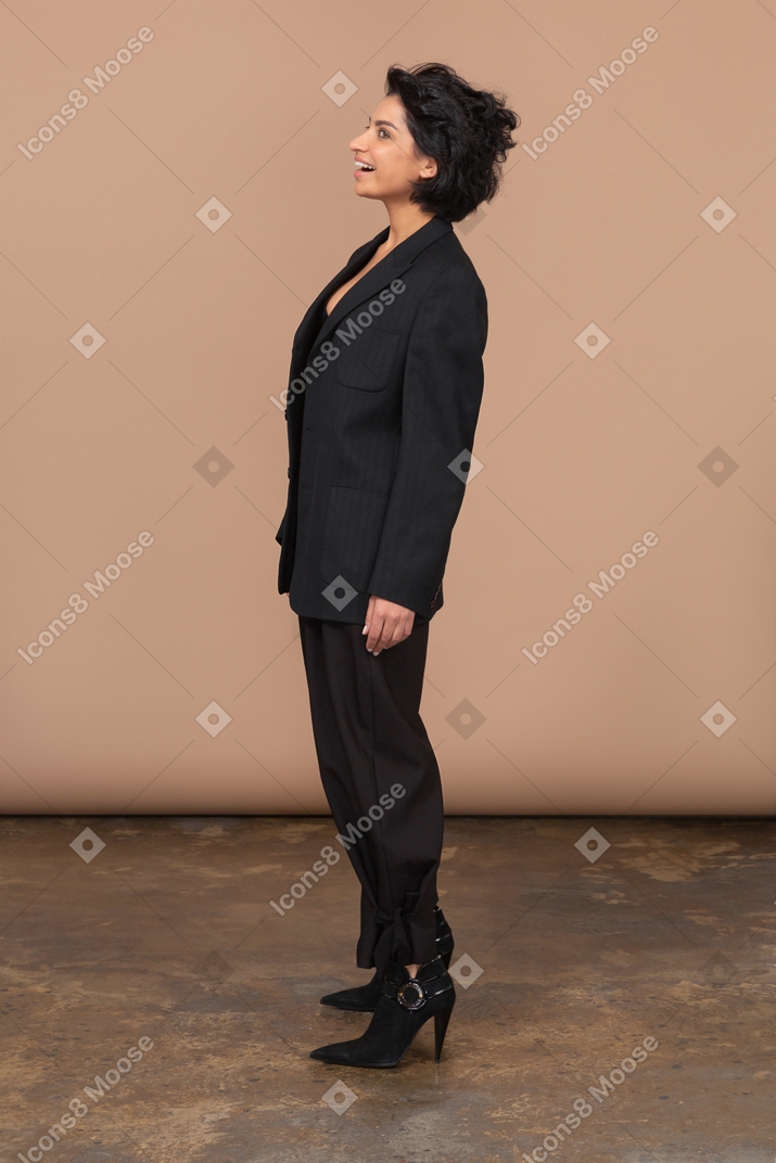 Вид сбоку удивленной улыбающейся бизнес-леди в черном костюме