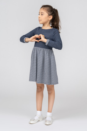 A little girl in a blue dress making a heart with hands