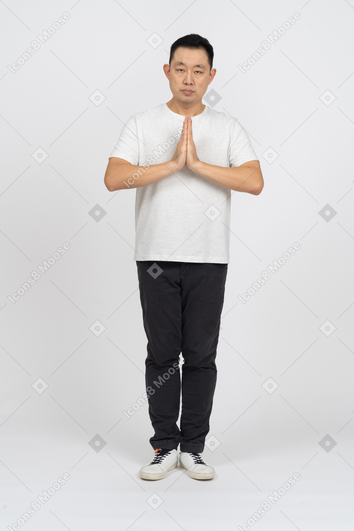 Vista frontale di un uomo in abiti casual che fa un gesto di preghiera e guarda la fotocamera