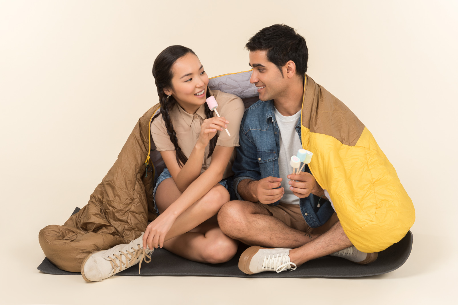 Young interracial couple sitting in sleeping bag and holding marshmallows