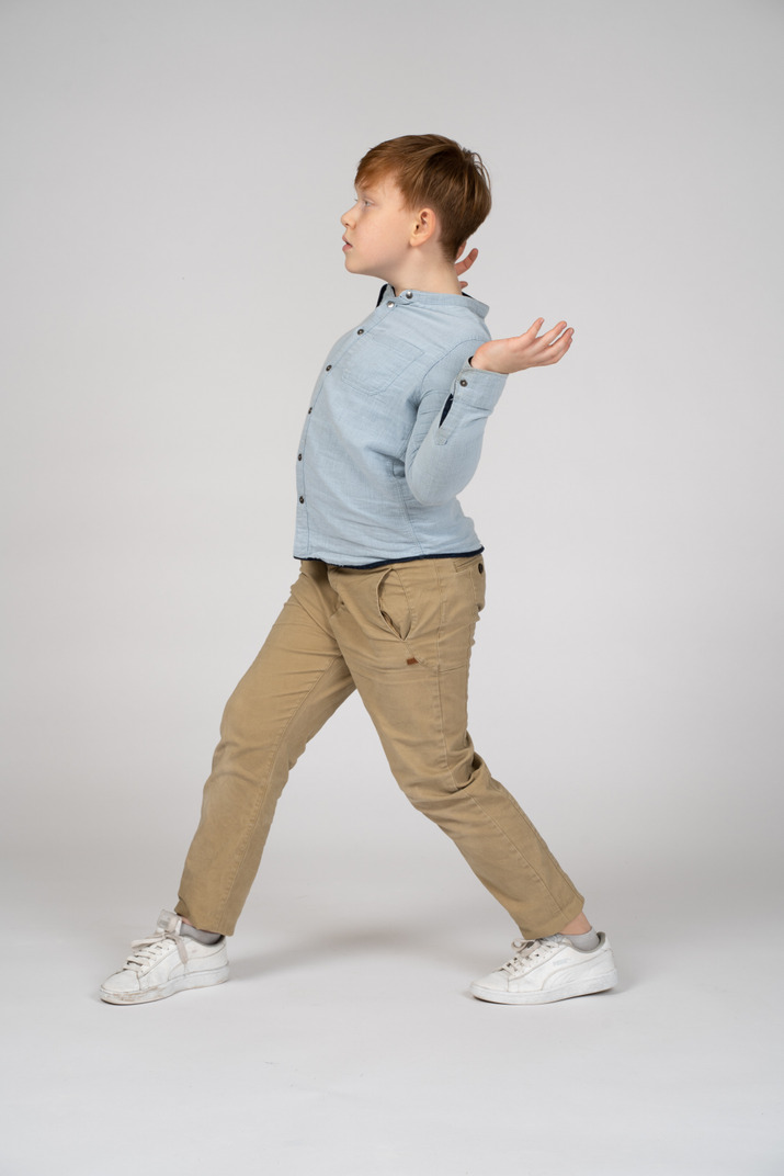 A boy standing in front of a wall with his legs crossed