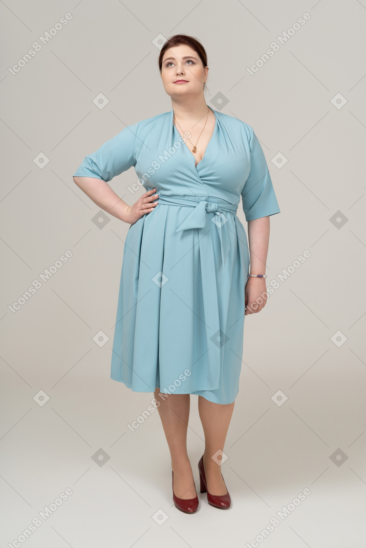 Вид спереди женщины в синем платье позирует с рукой на бедре