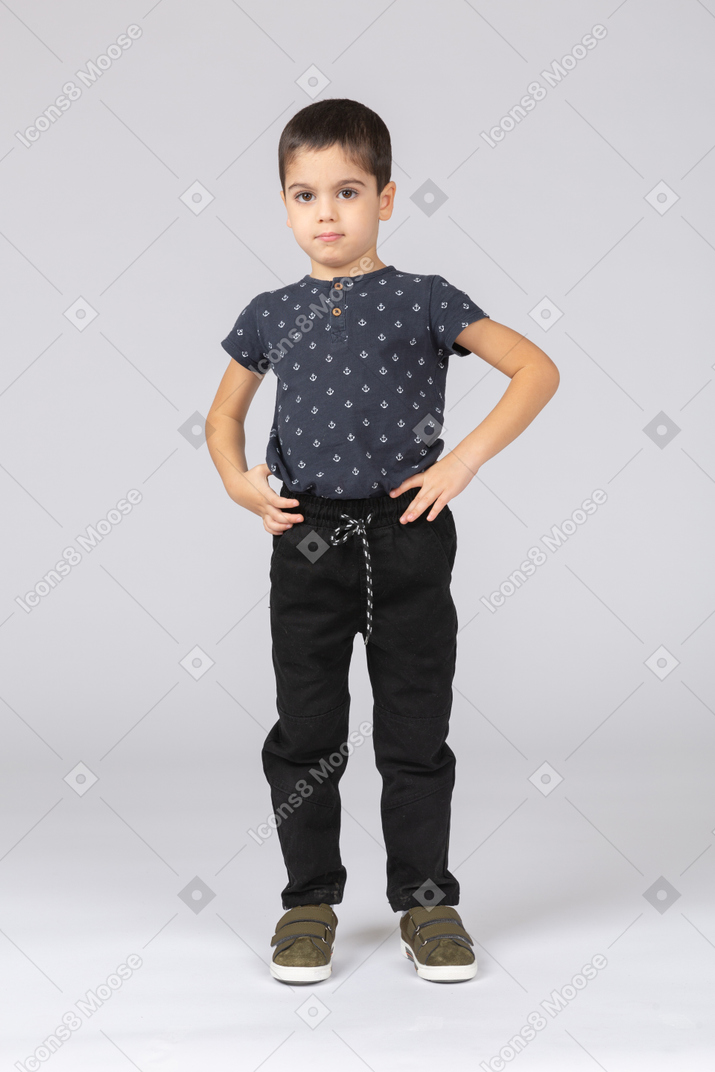 Front view of a cute boy posing with hands on hips and looking at camera
