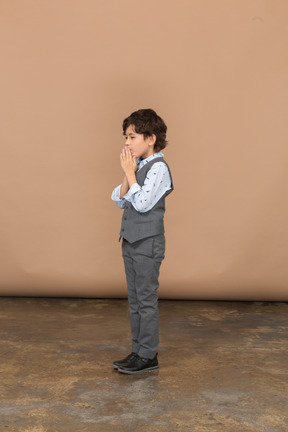 Vista laterale di un ragazzo in giacca e cravatta che fa un gesto di preghiera