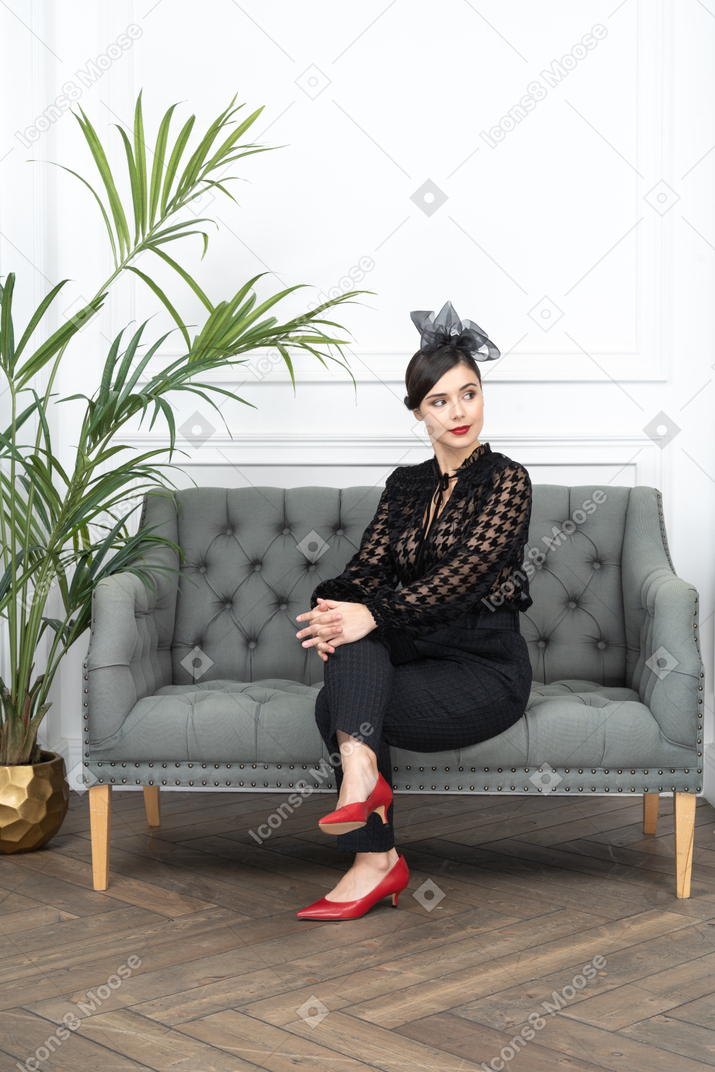 A woman sitting on a couch next to a potted plant