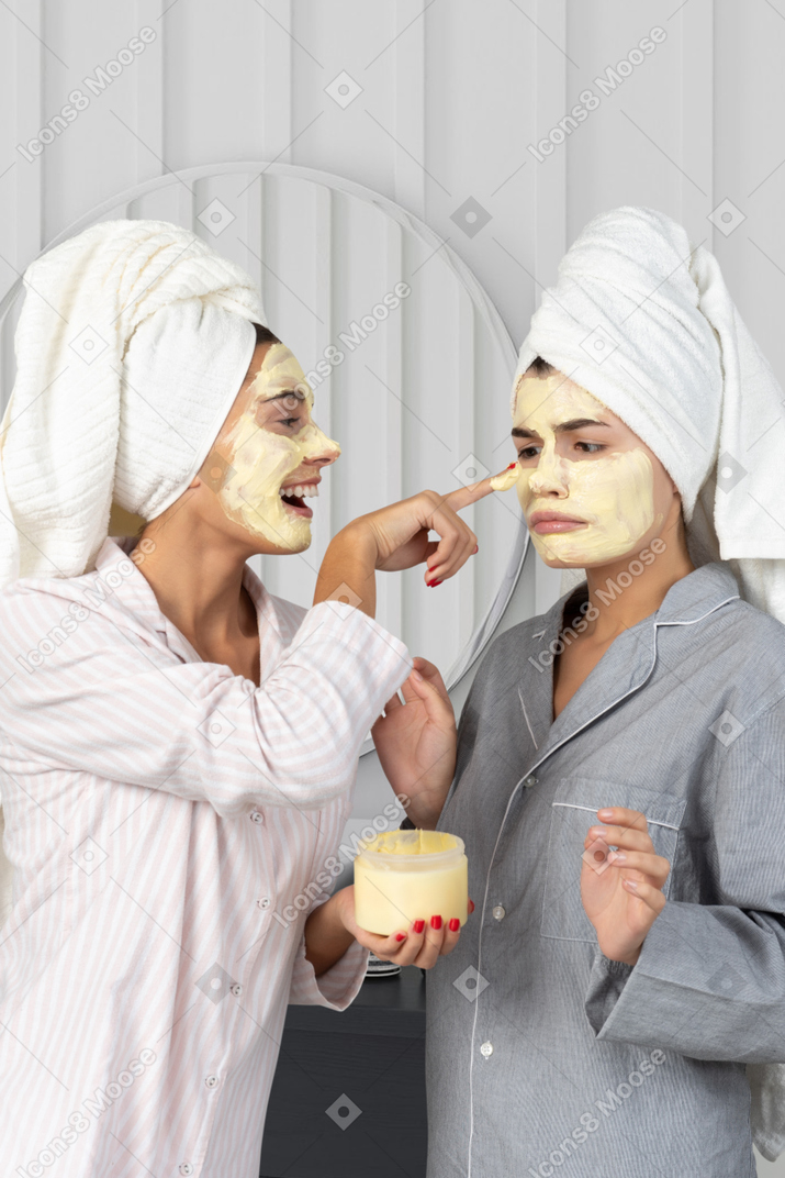 A young woman applying facial mask on another woman's face