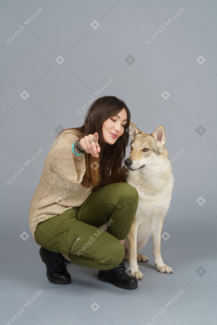 Full-length of a female master pointing at camera and looking at her dog