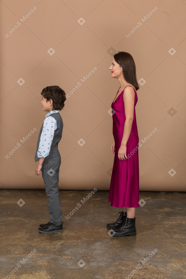 身着红色连衣裙的 stylsih 女人和身着西装背心的男孩站在侧面