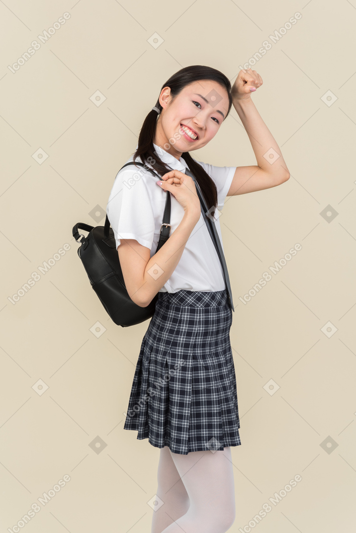 Asian school girl with backpack standing in profile and holding fist next to her forehead