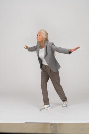Vista lateral de uma senhora idosa de terno em pé com os braços estendidos