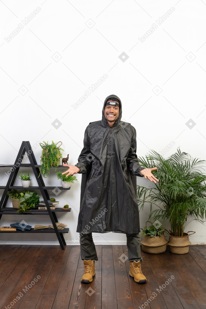 Homem sorridente com capa de chuva, encolhendo os ombros e abrindo os braços