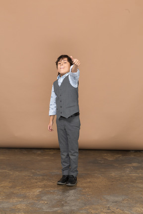 一个穿着灰色西装的可爱男孩竖起大拇指的正面图