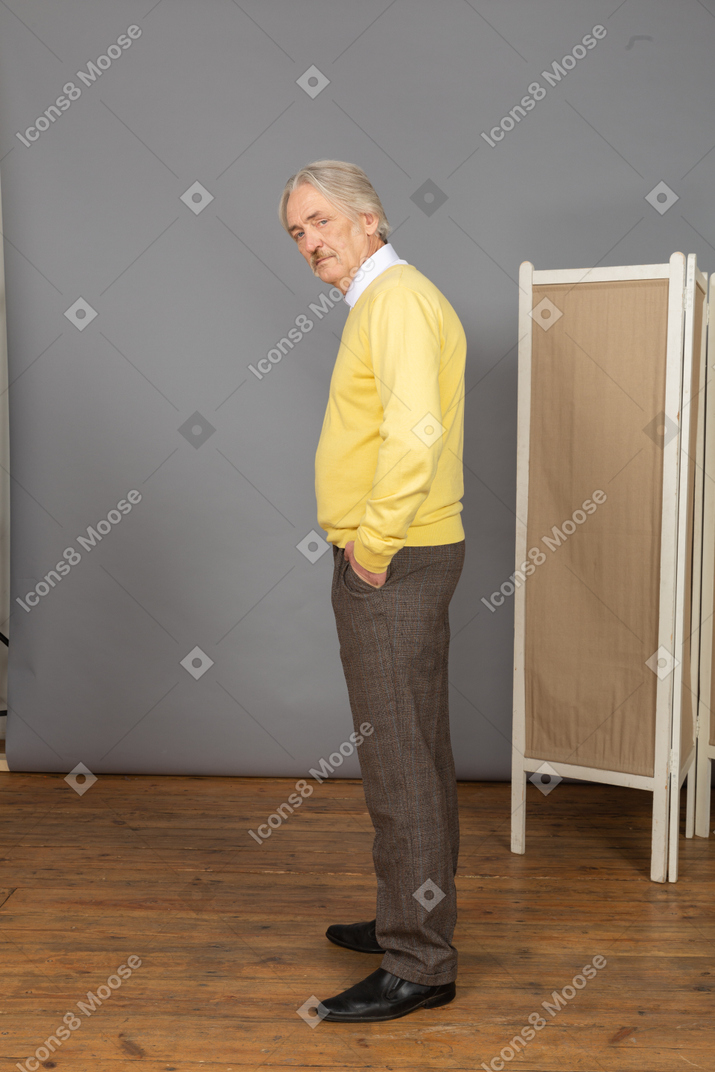 Side view of a serious old man putting hand in pocket while looking at camera
