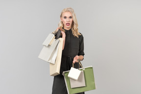 A young beautiful blond-haired person in a black dress holding a bunch of shopping bags in both of their hands