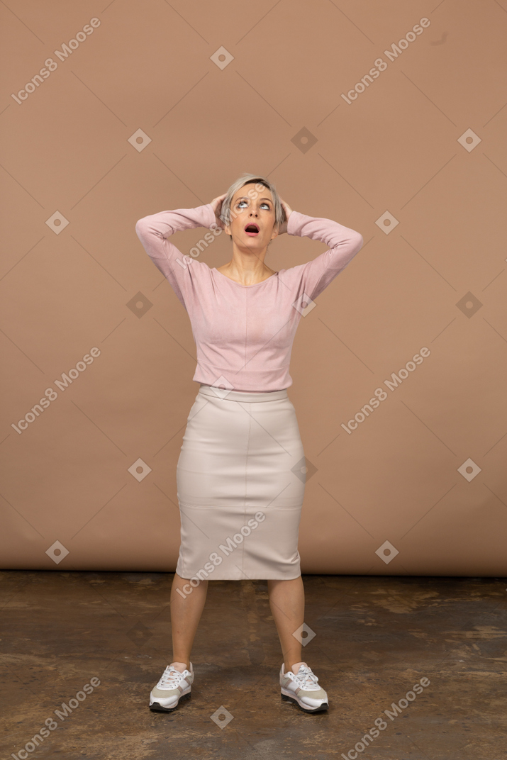 Vista frontal de uma mulher com roupas casuais em pé com as mãos atrás da cabeça