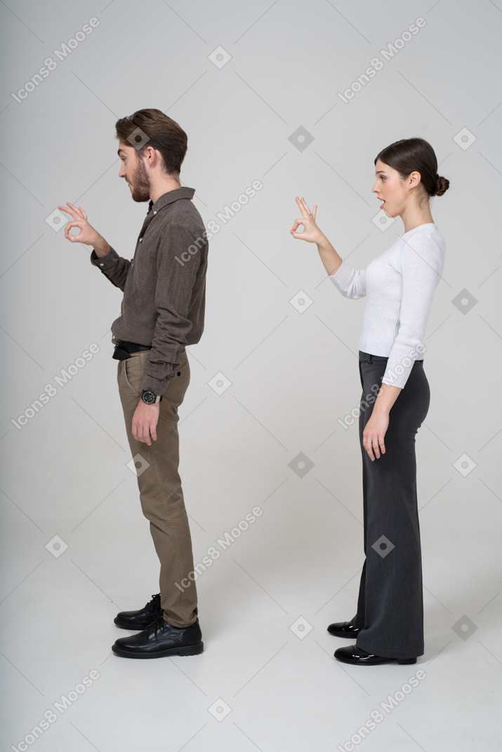 一对年轻夫妇在办公室服装显示ok的手势的侧视图