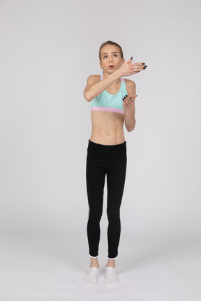 Vue de face d'une adolescente en tenue de sport, levant les mains et faisant valoir