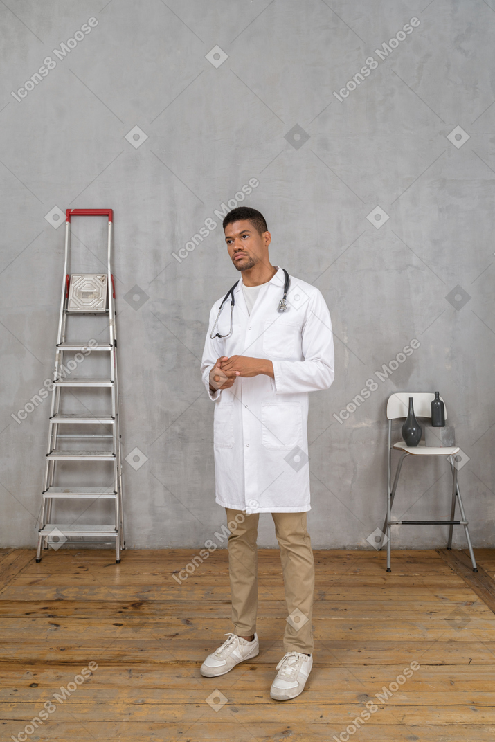 Vista di tre quarti di un giovane medico in piedi in una stanza con una scala e una sedia che si tengono per mano