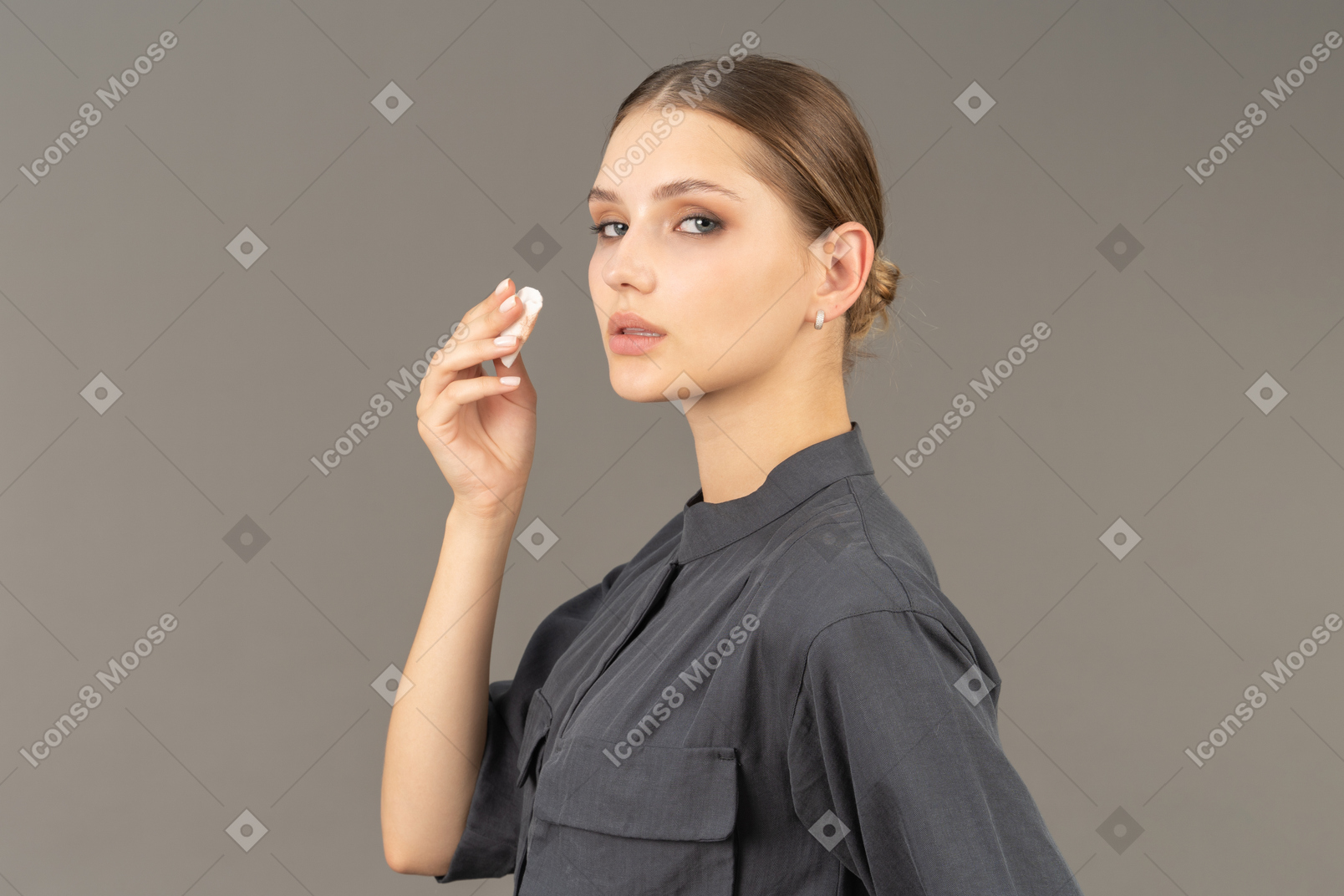 Vista lateral de uma jovem com um macacão removendo a maquiagem dos olhos