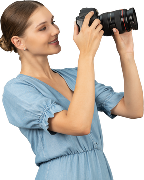 Vista di tre quarti di una giovane donna sorridente in abito blu che scatta una foto