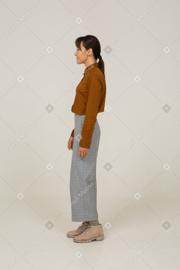 Side view of a young asian female in breeches and blouse standing still and pressing lips