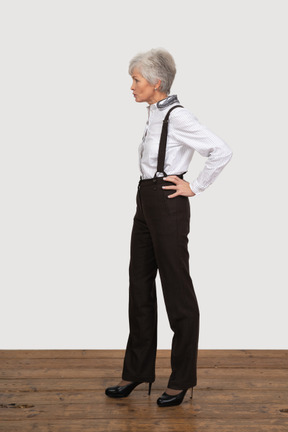 Side view of a displeased old lady in office clothing putting hands on hips