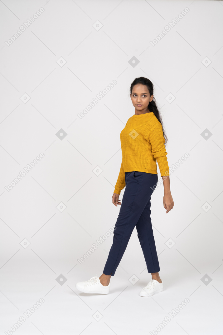 Side view of a girl in casual clothes walking and looking at camera