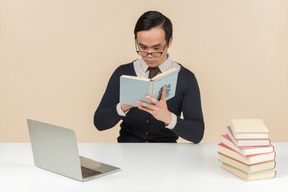 Junger asiatischer student in einer strickjacke ein buch lesend