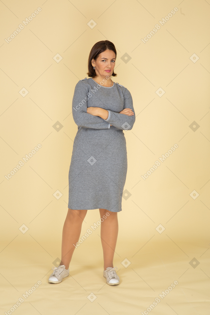 Vista frontal de uma mulher de vestido cinza posando com os braços cruzados