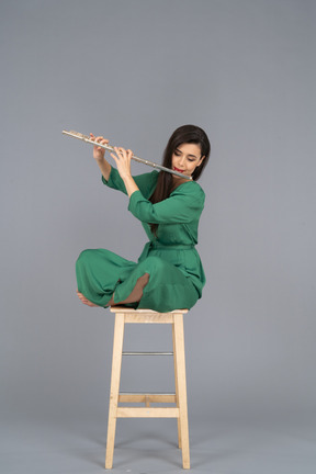 Full-length of a young lady playing the clarinet sitting with her legs crossed on a wooden chair