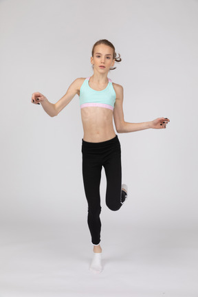 Front view of a teen girl in sportswear raising leg and outspreading hands