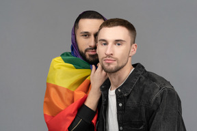 Nahaufnahme eines jungen mannes, der in eine lgbt-flagge gehüllt ist und hinter einem anderen jungen mann steht