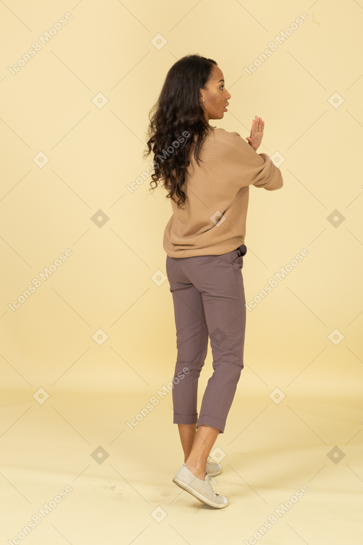 Three-quarter back view of a dark-skinned young female crossing hands