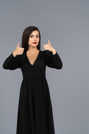 Vista frontale di una giovane donna in un abito nero che mostra i pollici in su