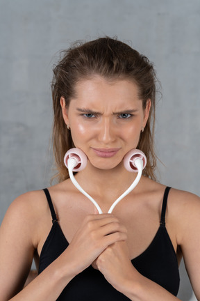 Close-up of a young woman using face roller while looking displeased