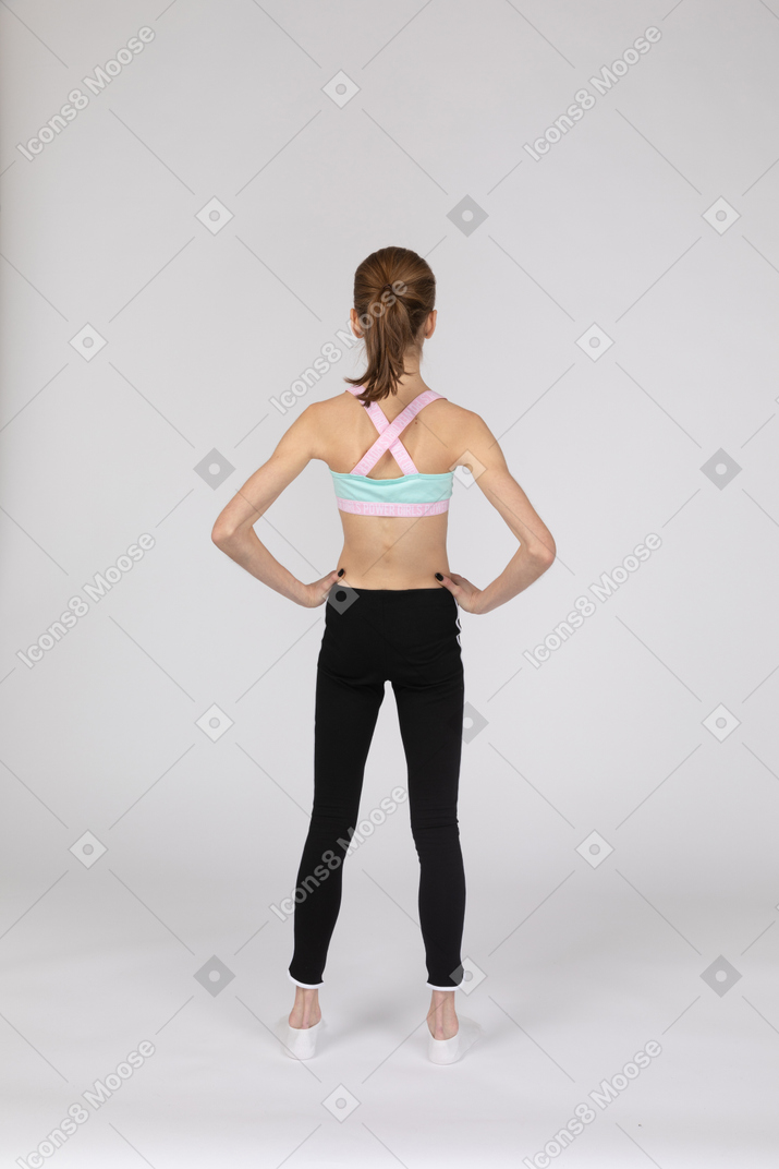 Vista posteriore di una ragazza adolescente in abiti sportivi che mette le mani sui fianchi