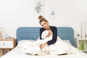 ベッドにとどまる毛布とパジャマで疲れた若い女性の正面図