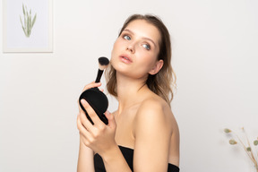 Side view of a young woman applying face powder while holding a mirror