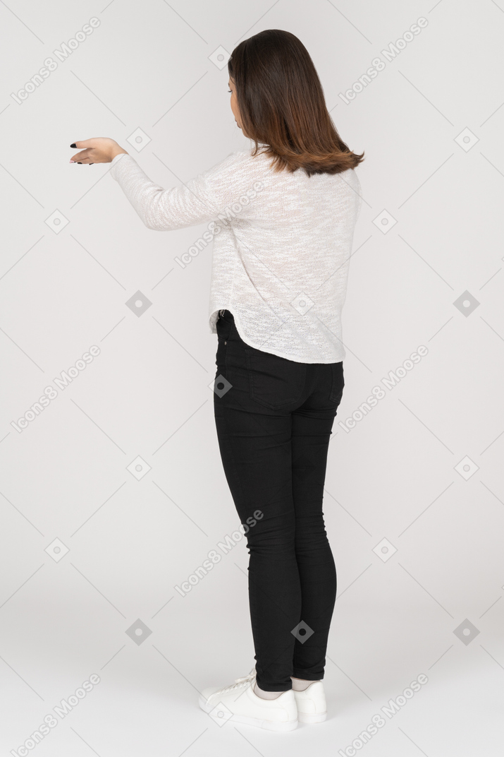 Three-quarter back view of a questioning young indian female in casual clothes raising hand