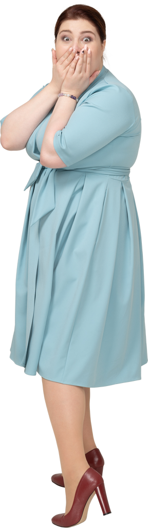 Vista lateral de una mujer sorprendida en vestido azul tapándose la boca con las manos
