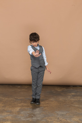 Vista frontal de um menino de terno cinza mostrando o gesto de parada