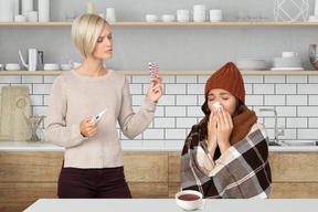 Woman giving pills and thermometer to sick friend
