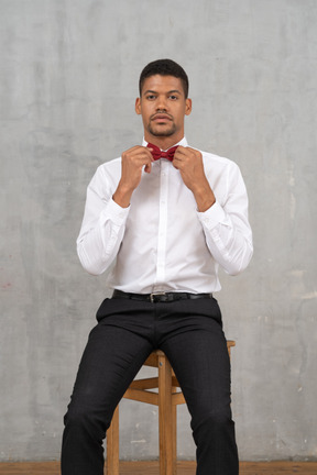 Young man sitting on a chair adjusting his bow tie